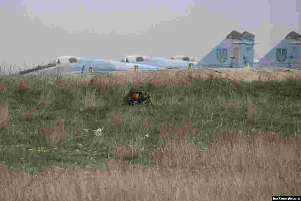 A Russian soldier watching Ukrainian military personnel at the Belbek airport, near Sevastopol. The Ukrainian Air Force base became one of the last Ukrainian holdouts in Crimea as its commander refused to hand over the site to Russian troops. He was eventually detained by Russian forces and Ukrainian personnel were forced out.&nbsp;