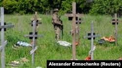 Вооруженный военный дежурит на кладбище во время захоронения останков российских военнослужащих. Луганск, подконтрольная России часть Украины, 18 мая 2023 года