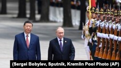 Președintele chinez Xi Jinpin (stânga) și președintele rus Vladimir Putin salută garda de onoare în timpul vizitei liderului rus la Beijing de anul trecut. 