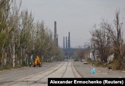 На вулиці тимчасово окупованого Маріуполя працює екскаватор, вдалечині видно металургійний завод «Азовсталь», що був зруйнований російськими обстрілами, листопад 2022 року