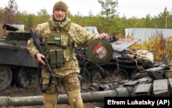 Военнослужащий Украины показывает эмблему элитного подразделения войск России возле уничтоженных российских танков в селе Дмитровка под Киевом, 2 апреля 2022 года