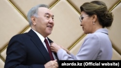 Дарига Назарбаева, спикер сената парламента, прикрепляет к лацкану пиджака своего отца Нурсултана Назарбаева нагрудный знак «Почётный сенатор». Нур-Султан, 6 июня 2019 года.  