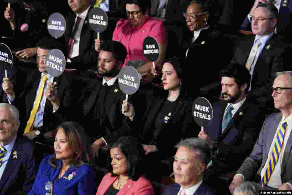 Члени Конгресу тримають плакати під час виступу президента Дональда Трампа на спільному засіданні Конгресу в Капітолії у Вашингтоні, 4 березня 2025 року.Написи на плакатах: «Маск краде», «Врятуй медичну допомогу». Також чимало конгресменів прийшли на засідання у краватках чи з брошками синьо-жовтого кольору на знак солідарності з Україною