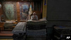 یک فروشنده منتظر است تا تخته‌های فرش خود را در گوشه‌ای تاریک از بازار بفروشد