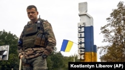 Український військовий біля знаку з написом «Куп’янськ» у відвойованому напередодні ЗСУ місті Куп’янську на Харківщині, 14 вересня 2022 року, ілюстративне фото