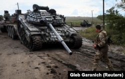 Українські військовослужбовці вантажать трофейний російський танк на вантажівку. Біля міста Ізюму на Харківщині, 24 вересня 2022 року