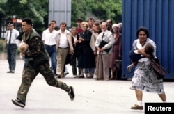 Солдат боснийской армии и боснийская женщина бегут через перекресток, по которому стрелял сербский снайпер. Оба несут на руках маленьких детей