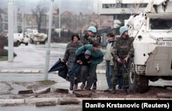 Жители Сараево укрываются от снайперского огня за бронемашиной Сил ООН по охране (СООНО) на этом архивном фото 1993 года