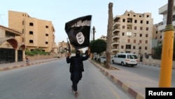 Боевик "Исламского государства" со знаменем группировки на улице сирийского города Ракка, фактической столицы халифата, провозглашенного ИГ