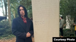 Наталья Садықова Францияның Байе қаласындағы журналистерге арналған мемориалда тұр. Мемориалға 9 қазанда күйеуі, журналист Айдос Садықовтың есімі енгізілген. Сурет Садықованың парақшасынан алынған. 