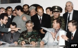 Секретар Ради безпеки Росії Олександр Лебідь (другий справа) передає підписаний документ представнику ОБСЄ в Хасавюрті, коли командир чеченських повстанців Аслан Масхадов (посередині) готується підписати знакову мирну угоду між Ічкерією та Росією. 30 серпня 1996 року