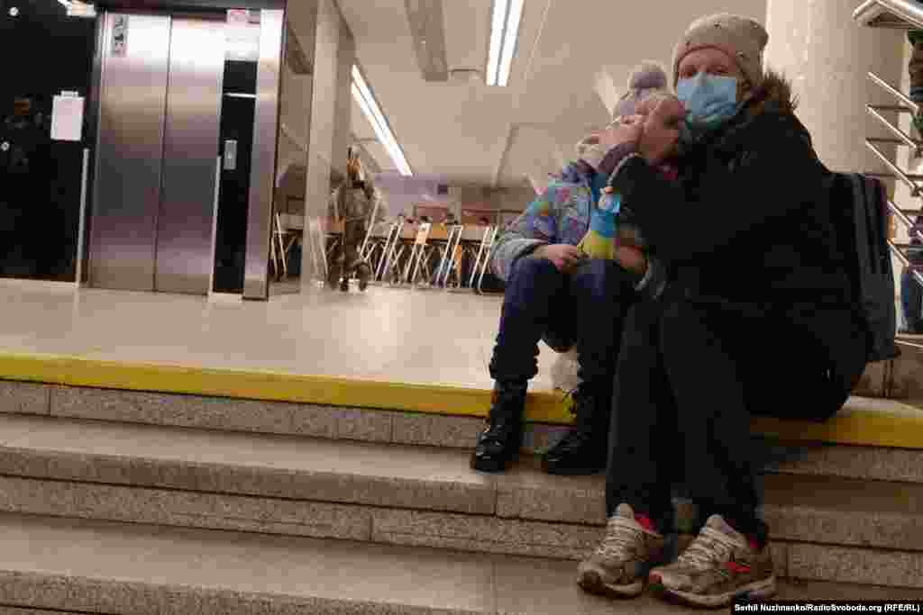 Жінка обіймає дитину, ховаючись від обстрілів на станції метро «Голосіївська», Київ, 24 лютого 2022 року.Перші години повномасштабного вторгнення: одні люди ще звично їдуть у метро у справах, а інші вже поспішають із валізами виїхати з міста. 