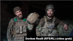 Военнослужащий с позывным «Гром» демонстрирует свою каску, в которую попала российская пуля. Рядом стоит боец с позывным «Мелкий»