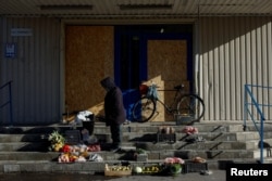 Жінка продає овочі на сходах біля закритого супермаркету, 28 жовтня 2023 року