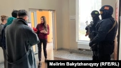 Orda.kz редакциясы есігінің сыртында тұрған қарулы полиция қызметкерлері мен заңгер Ольга Диденко (ортада). Алматы, 1 желтоқсан, 2025 жыл.