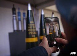 Мужчина фотографирует 155-мм боеприпасы на месте будущего артиллерийского завода, где немецкий производитель оружия Rheinmetall планирует начать производство с 2025 года, в Унтерлюссе, Германия, 12 февраля 2024 года
