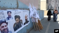 Afghan women walk by posters of Taliban leaders and flags in Kabul, Afghanistan, in August 2021.