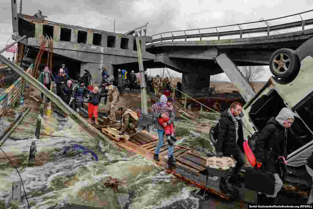 Цивільні, несучи на руках дітей, переходять річку по дерев’яній кладці під підірваним мостом на межі між Ірпенем і житловим масивом Романівка. Березень 2022 року. До 2022 року, за даними УВКПЛ ООН та українських правоохоронців, внаслідок бойових дій загинули 152 дитини, 146 були поранені