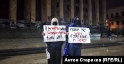 Молодая пара с плакатами подшучивает над силовиками, использующими водометы. Грузия, декабрь 2024 года