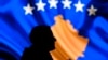 A man stands in front of a screen displaying the Kosovo flag in Pristina.