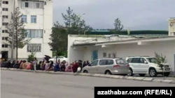 Люди сидят неподалеку от магазина в ожидании начала продажи продуктов питания. Государственный магазин №4 в 11-м микрорайоне Ашхабада. Май, 2021